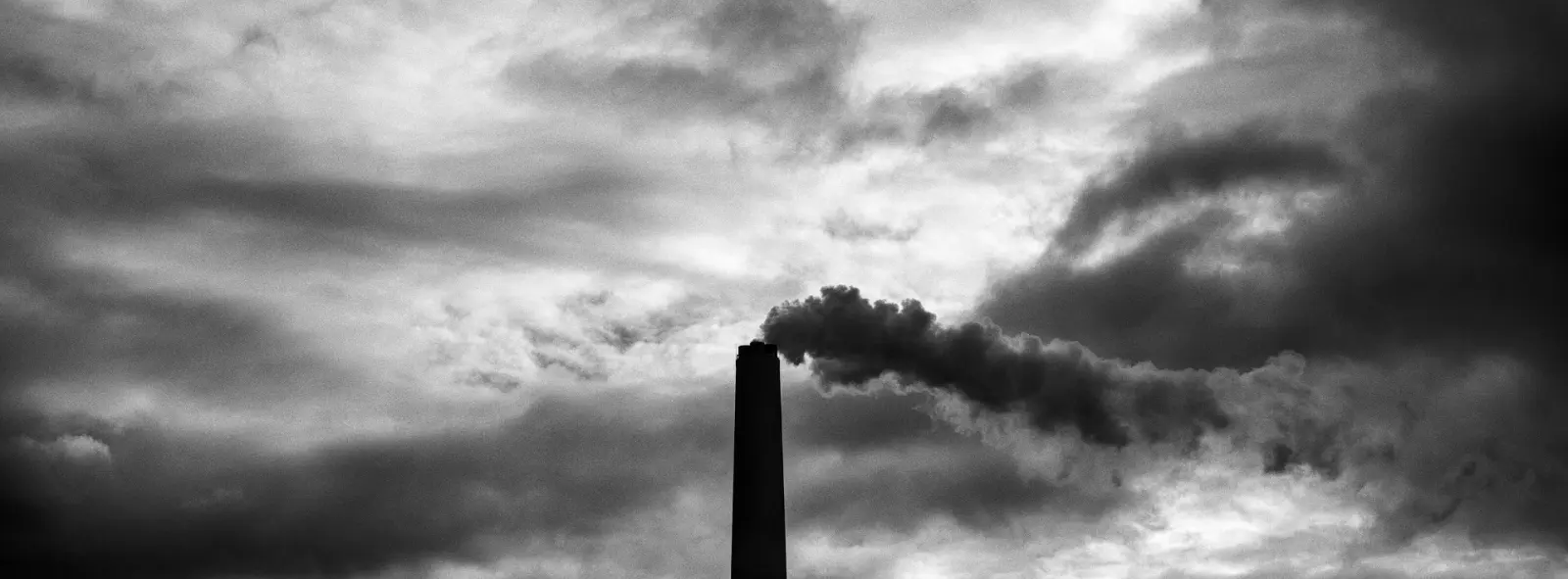 Smokestack of a coal-fired power plant silhouetted against a sky in transition